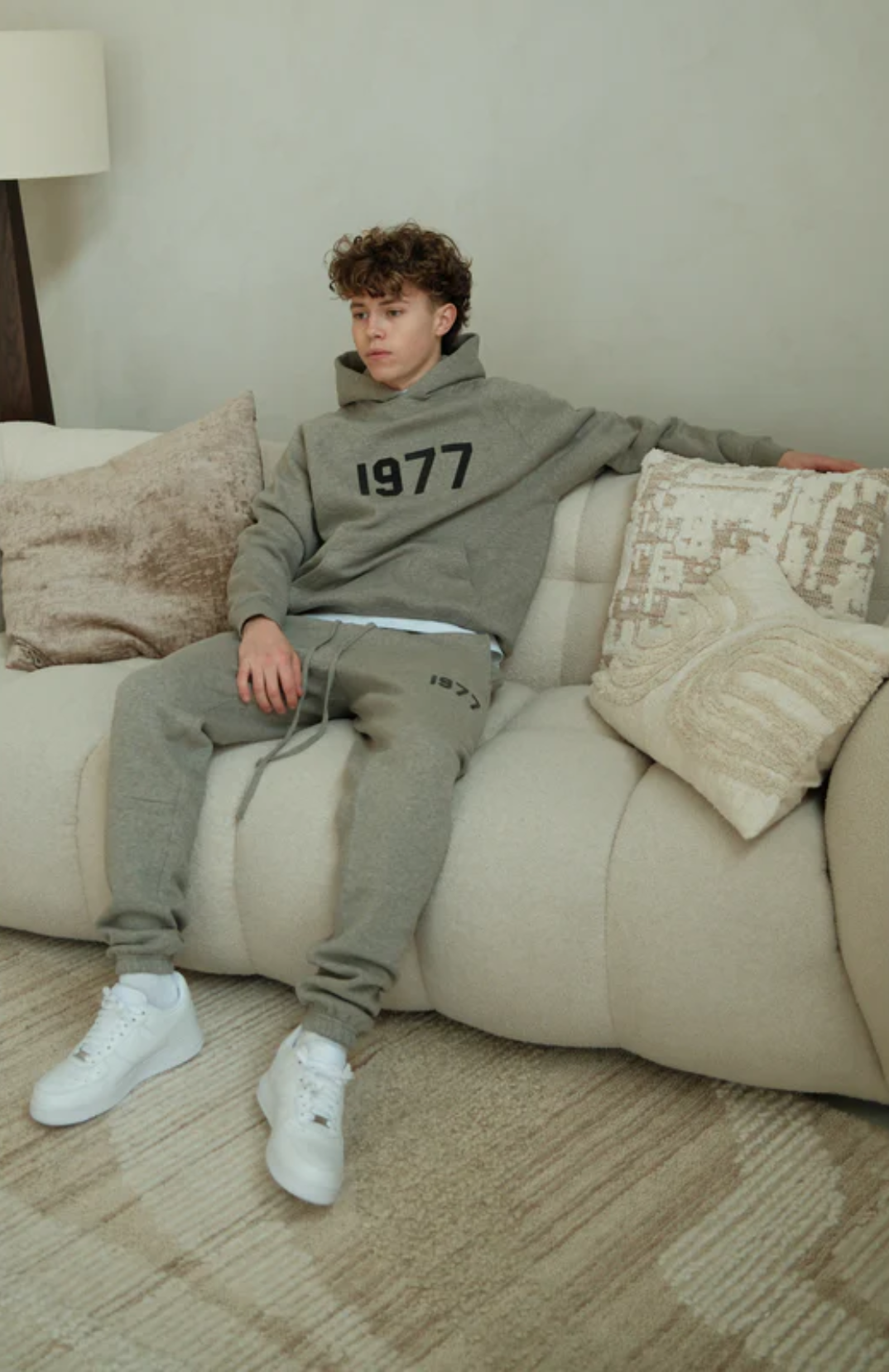 Fear of God ESSENTIALS 1977 hoodie and sweatpants set in dark oatmeal worn by model sitting